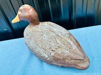 Side angle photo showing the textured brown body, painted head, and yellow wooden beak of the decoy.