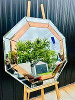 Front view of vintage hexagonal mirror showing the alternating silver and bronze tone mirrored panels reflecting outdoor scenery.