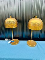 Pair of vintage Mid-Century Modern table lamps with pierced dome-shaped gilded metal shades against a panelled dark background.