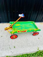 Photo showing full view of the vintage wooden child's wagon, green painted bed, metal red wheels and yellow handle with blue/white grip.
