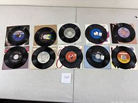 Ten assorted 45rpm vinyl records arranged in two rows with various labels and some original paper sleeves.