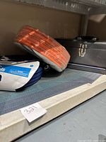 Orange coiled Amflo multi-purpose PVC air hose and blue light duty garden hose on shelf.