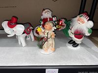 Four Annalee felt dolls including two Santa Claus figures, elf doll, and a white elephant on display.