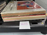 Side view of stack of 16 assorted vinyl albums showing album spines with various titles and labels.