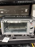 Front view of Black and Decker toaster oven on a shelf with cooling rack on top and a baking tray inside, showing overall appearance and size.