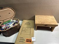 Small wooden stool, boxed wooden book rack, and vintage plastic sewing box on table.