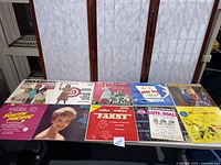 Ten assorted Broadway musical vinyl records displayed on a black surface showing titles like South Pacific, Guys and Dolls, Fanny, and others.