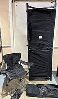 Folded black camping cot with carrying case and unfolded black camping chair in front