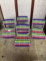Set of four children's chairs with multicolor woven seats and backs arranged on carpet with visible concrete floor and wall paneling background.