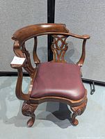 Front left angle view of Chippendale style corner chair showing burgundy leather seat and wood carved legs.