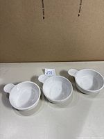 Three white CorningWare Grab-It bowls arranged side by side on a surface showing slight scratches.