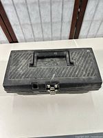 Closed black Durabull toolbox with carry handle and metal latch, shows surface dust and wear