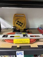 Yellow portable power cord reel, level resting on a box, and the coiled orange extension cord beneath it
