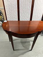 Full view of the card table showing the mahogany finish and shape with shadows from the lighting.