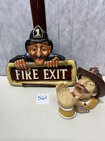 Fire Exit sign held by fireman figurine with mustache and helmet.