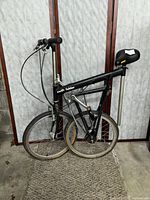 Side view of the folded black Swift Folder folding bike with 20-inch wheels, folded compactly and leaning against a decorative screen.