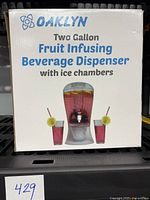 Box front showing brand name Oaklyn, product name, and illustration of dispenser with two glasses containing beverages with lemon slices and straws.