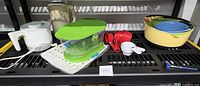 Overview of items on black shelving with hot pot, bowls, measuring cups, vegetable container, thermometer, and protector mat.