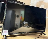 Front view of the LG 32" tabletop TV showing screen and stand, with lot sticker visible.
