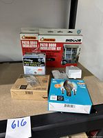 Full lot overview showing all items arranged on a cardboard surface: Frost King patio door insulation kits (2 boxes), Rite Lite motion LED safety light in packaging, shrink film roll, electrical sensor plug, and Ecosmart LED bulb boxes.