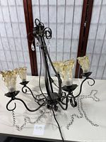 Full chandelier showing wrought iron frame, four yellow-tinted hand blown glass light shades, and hanging crystal beads and pendants.