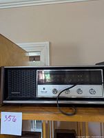 Front view of Panasonic RE-7369 radio showing black speaker grill, tuning window, control knobs and power cord.