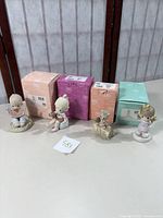 Four Precious Moments figurines displayed with their original boxes behind them, showing the full set titled Water-Meloncholy Day Without You, You're a Gem of a Friend, A Chip Off The Old Block, Grandma's Little Angel