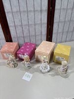 Four Precious Moments figurines displayed in front of their original boxes, showing the full collection.
