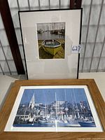 Two framed photographic prints, one showing yellow boat on sand and the other a marina scene with sailboats and church steeple