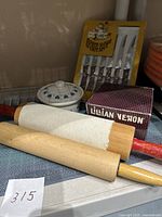 Two wooden rolling pins with red and natural handles, vintage ceramic canister with lid, Lillian Vernon box, and six-piece steak knife set package visible.