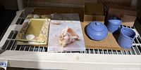 Two seashell photo frames, seashell canvas picture, and set of three blue sugar/creamer ceramic items on a shelf.