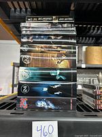 Stack of DVD boxes for seasons 1 to 8 of 24 TV series with 24 Declassified Trinity novel on top, showing front cover artwork and titles.