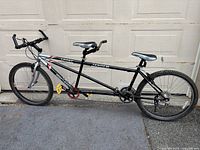 Full side profile of black and silver tandem bicycle leaning against garage door