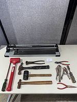 Manual tile cutter alongside assorted hand tools including hammers and pliers
