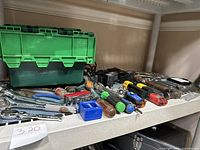 Wide shelf view showing green toolbox, assorted hand tools including wrenches and screwdrivers.
