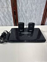 Closed Toshiba Satellite L655 laptop with power adapter and two Memorex mini external speakers on top