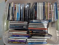 Top down view of large collection of used CDs stacked and arranged in a plastic bin. Titles visible include some classic and popular music albums from various artists.