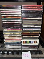 Stacked assorted used music CDs showing various artist titles on spines and cases.