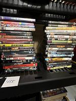 Two stacks of assorted used DVDs including various movie titles on a black metal shelf.