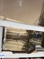 Photo of a smaller decorative cast frame mirror with a beveled edge and etched design, placed on a white shelf with other mirrors nearby.