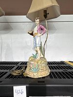 Full view of vintage porcelain figural lamp showing young man figure, lamp shade, and electrical cord.
