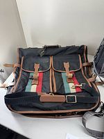 Front view of vintage Lark black garment bag showing leather trim, multicolor stripes, buckle pockets, and adjustable straps.