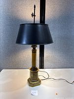 Photo showing full lamp with yellow and gold toleware base and black tapered shade, lamp is turned off.
