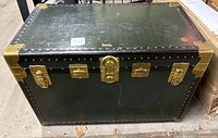 Front view of vintage Vacationer vulcanized fiber trunk showing green body, brass hardware and latch lock.