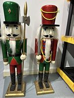 Two large wooden nutcrackers side by side on the floor, one green and red, the other red and green, showing their full height and details.