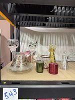 Set of Christmas themed glass candle holders including two glass angel votive holders (one gold and one silver), two crackle glass candle holders, three small votive holders, a red round glass votive holder, and one green votive holder visible on shelf.