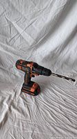 Side view of Black and Decker cordless drill with drill bit attached, placed against white fabric background.