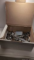 Open box view showing assorted sockets, socket wrench handles, wrenches, and bits inside.