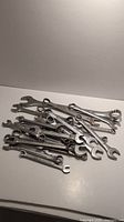 Photo showing a pile of combination wrenches in various sizes and brands on a white surface.