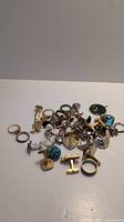 Top view of a collection of assorted cufflinks and rings in various metals and colors scattered on a white surface.